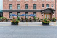 some tables with blue umbrellas and flower pots with flowers on them and yellow poles