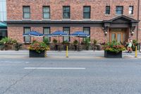 some tables with blue umbrellas and flower pots with flowers on them and yellow poles