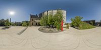 a panorama of an outdoor fountain with no grass in front of the building and trees