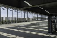 a walkway over looking a fence in an industrial setting with the sun filtering through the glass