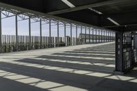 a walkway over looking a fence in an industrial setting with the sun filtering through the glass