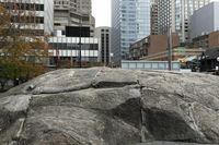 there is an artistic rock in the middle of a public square with tall buildings and skyscrapers