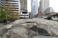 there is an artistic rock in the middle of a public square with tall buildings and skyscrapers