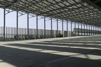 a long covered warehouse area with many large poles next to the walkways and fence