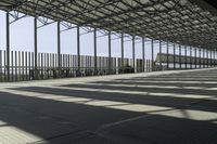 a long covered warehouse area with many large poles next to the walkways and fence