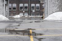 the empty parking lot has only snow on the ground in front of an old brick factory