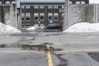 the empty parking lot has only snow on the ground in front of an old brick factory