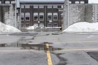 the empty parking lot has only snow on the ground in front of an old brick factory