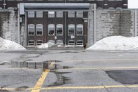 the empty parking lot has only snow on the ground in front of an old brick factory