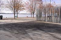 a sidewalk and boardwalk near the water near trees in the fall time, with two benches at the end