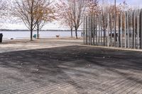 a sidewalk and boardwalk near the water near trees in the fall time, with two benches at the end