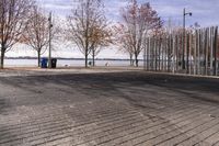 a sidewalk and boardwalk near the water near trees in the fall time, with two benches at the end