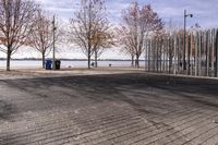 a sidewalk and boardwalk near the water near trees in the fall time, with two benches at the end