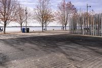 a sidewalk and boardwalk near the water near trees in the fall time, with two benches at the end