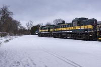 an empty train sitting on tracks with snow and trees in the background and cloudy skies