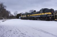 an empty train sitting on tracks with snow and trees in the background and cloudy skies