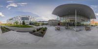 a fisheye image of the outside of a building with benches and picnic benches on the sidewalk