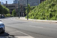 a car is traveling down the street next to a tall tree and building in the distance