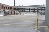 the empty parking lot has only snow on the ground in front of an old brick factory