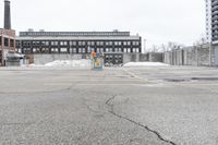 the empty parking lot has only snow on the ground in front of an old brick factory