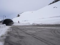 a snowy road with lots of snow on the ground near a tunnel with a snowman walking up it