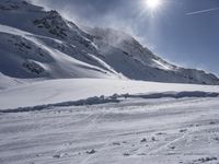 a skier walking on top of a snow covered slope near mountains and a sun glare