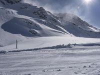 a skier walking on top of a snow covered slope near mountains and a sun glare