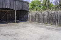 a wooden barn with some plants on the roof and outside wall next to a fence