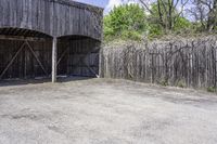 a wooden barn with some plants on the roof and outside wall next to a fence