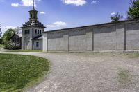 an empty concrete building near a grassy field in front of a large church tower and clock tower