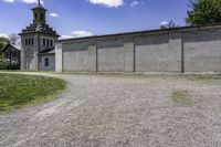 an empty concrete building near a grassy field in front of a large church tower and clock tower