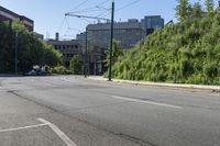 a street scene with focus on the road, trees and bushes, with buildings in the background