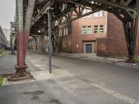 a street with two red brick buildings underneath a train bridge and a parking lot in front of it