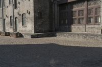 the person is walking down the street near old buildings on a sunny day with a red umbrella