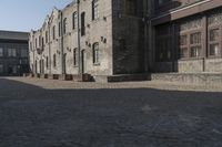the person is walking down the street near old buildings on a sunny day with a red umbrella