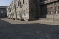 the person is walking down the street near old buildings on a sunny day with a red umbrella