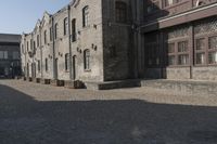 the person is walking down the street near old buildings on a sunny day with a red umbrella