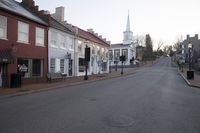 an empty street in a town with tall buildings on either side of it and a steeple on the horizon