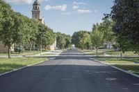 a view down the street of a town with many trees lining the sidewalks and steeples