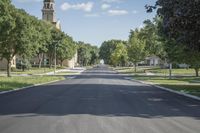 a view down the street of a town with many trees lining the sidewalks and steeples