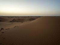 tracks are seen in the sand as the sun sets in the background and mountains appear in the distance