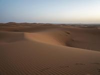 tracks are seen in the sand as the sun sets in the background and mountains appear in the distance