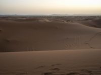 tracks are seen in the sand as the sun sets in the background and mountains appear in the distance