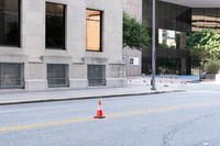 a traffic cone on the road in front of building and trees and street cones in the middle