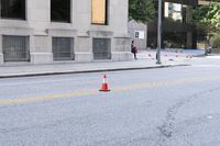 a traffic cone on the road in front of building and trees and street cones in the middle