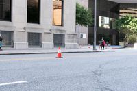 a traffic cone on the road in front of building and trees and street cones in the middle