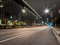 an empty city road lit with street lights at night, in front of a large building