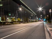 an empty city road lit with street lights at night, in front of a large building