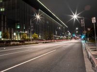 an empty city road lit with street lights at night, in front of a large building