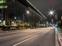 an empty city road lit with street lights at night, in front of a large building